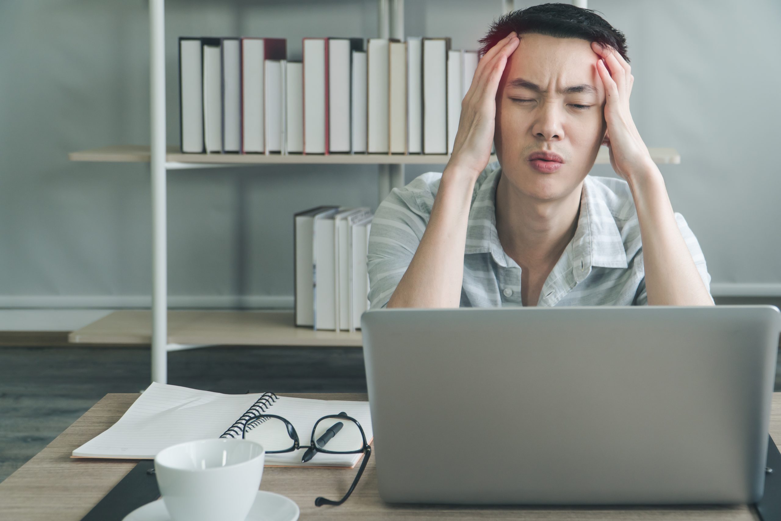 Freelance young man working on laptop and having a headache, tired, at home office. Businessman video call meeting with stress and seriousness. college students men sit learning online in library.