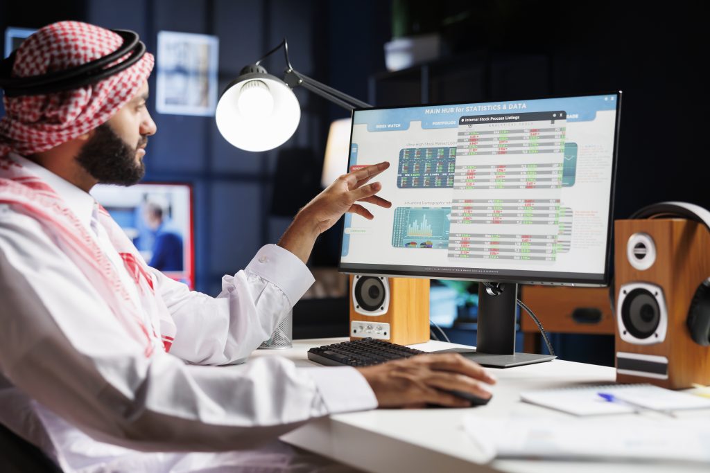 An Arab businessman diligently analyzing data on his computer, making important decisions for the company. Muslim guy wearing traditional attire is checking charts and data on his desktop pc.