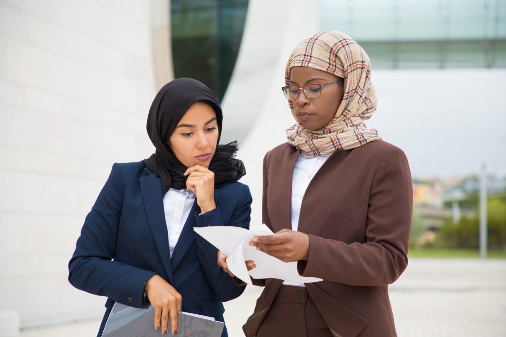 Serious Muslim business colleagues reviewing documents outside. Business women in hijabs standing outdoors and reading papers together. Paperwork concept
