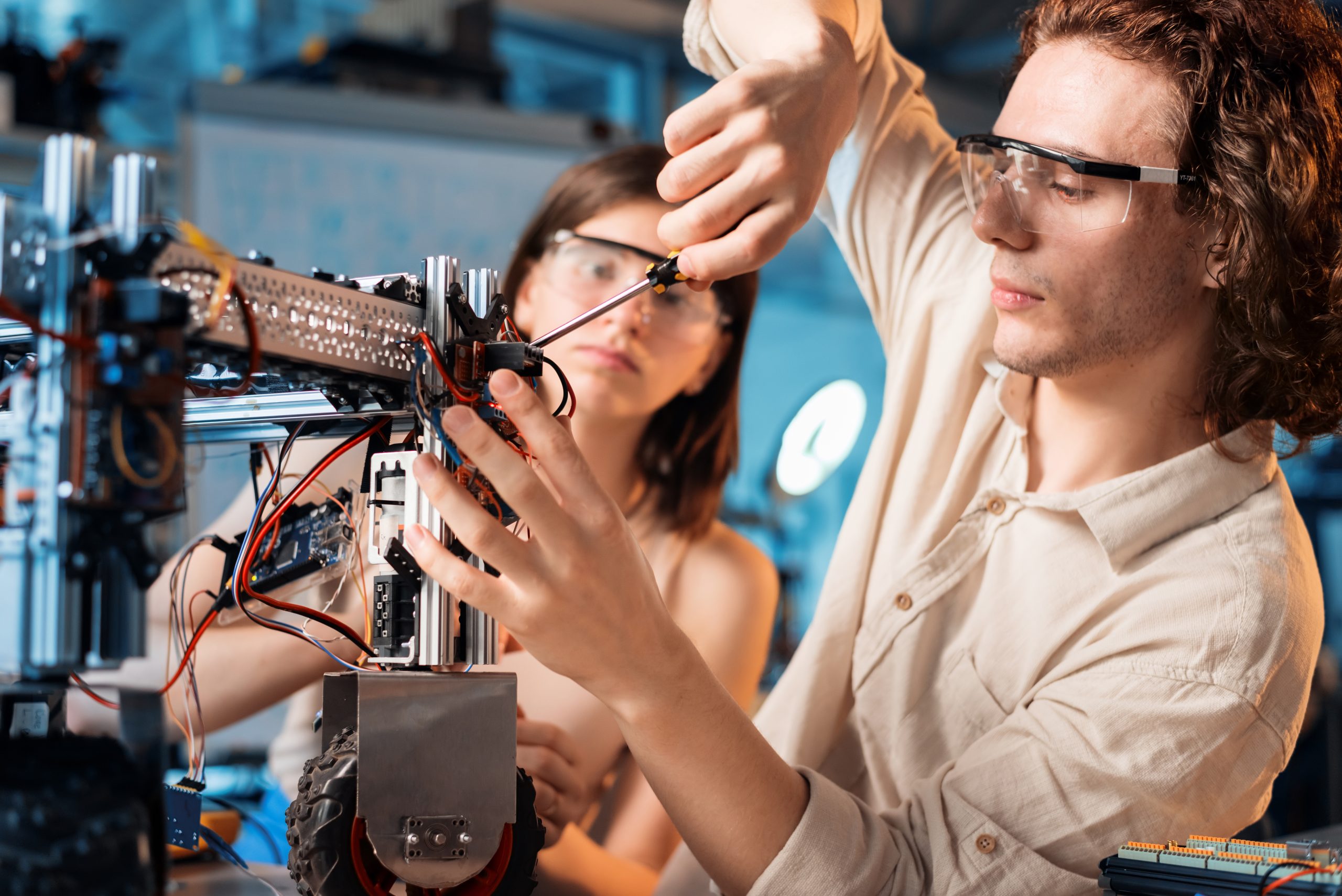 young man and woman in protective glasses doing experiments in robotics in a laboratory. Robot on the table